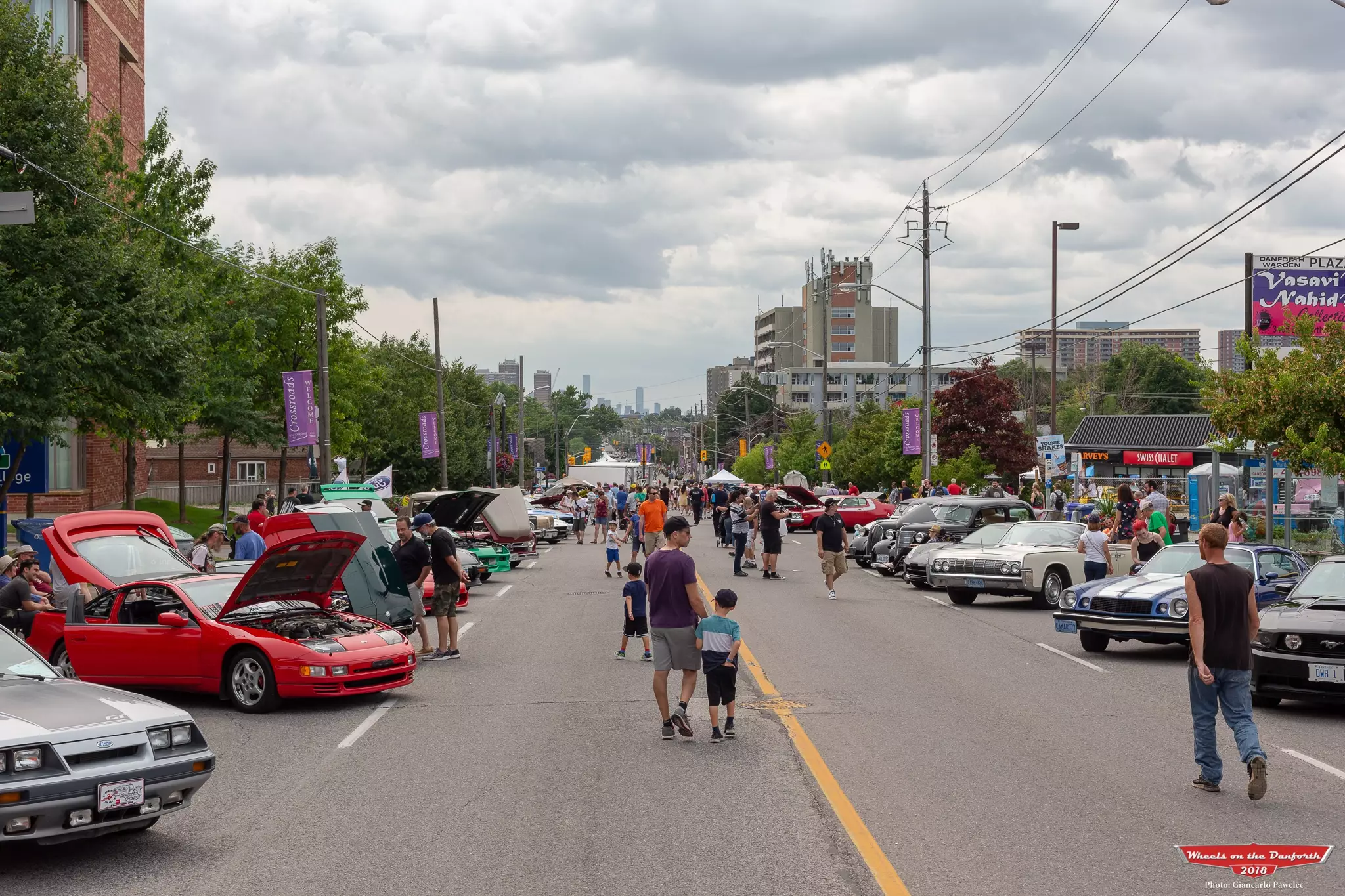 Wide shot of Wheels on the Danforth event with cars parked on each side and attendees walking.